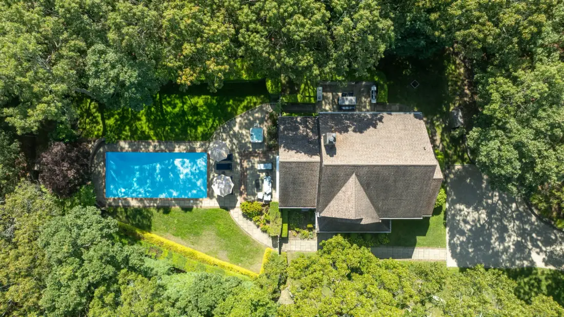 An aerial view of a house and swimming pool surrounded by dense greenery.