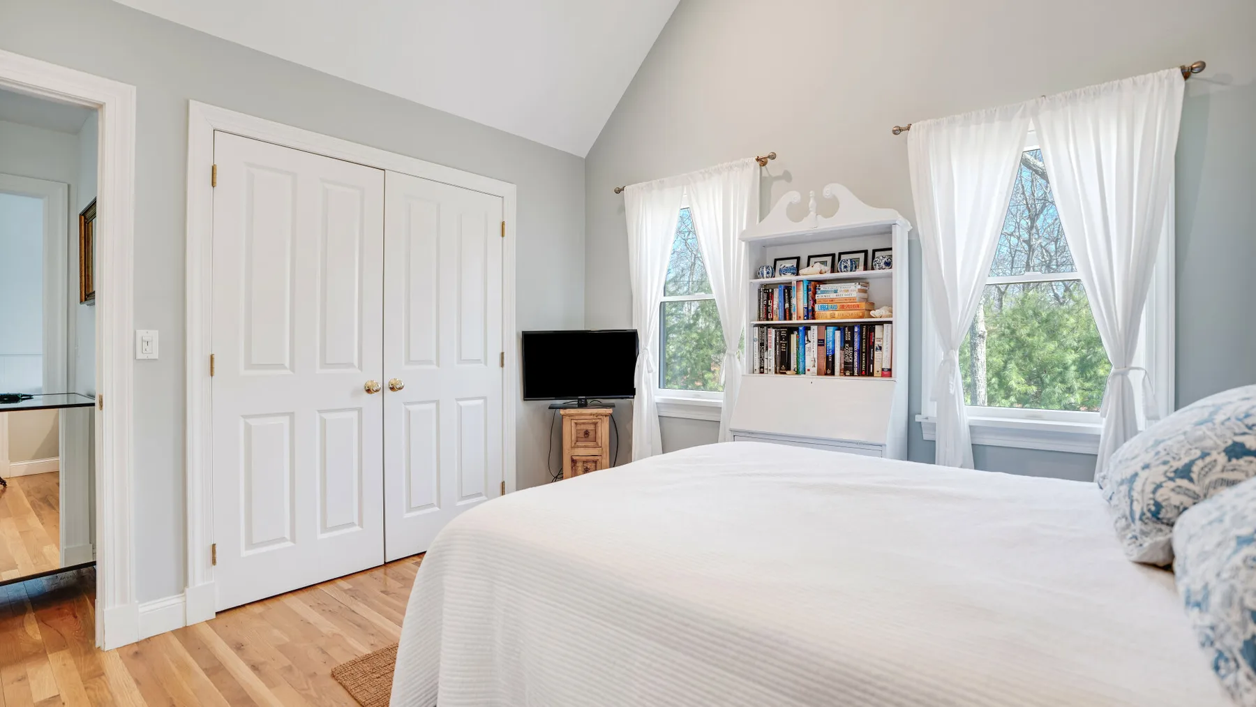 Un dormitorio luminoso con una cama grande, puertas blancas de armario y una estantería.