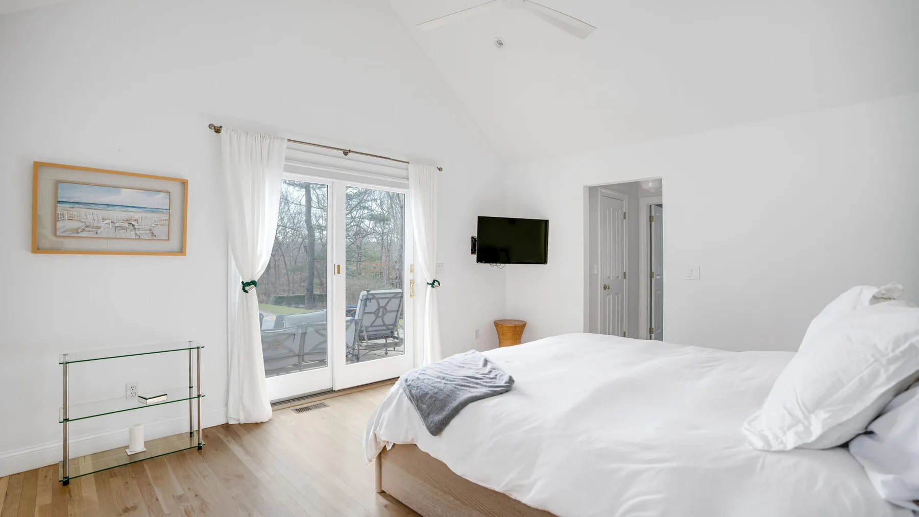 Un dormitorio luminoso con una cama, puertas de vidrio y un televisor en la pared.