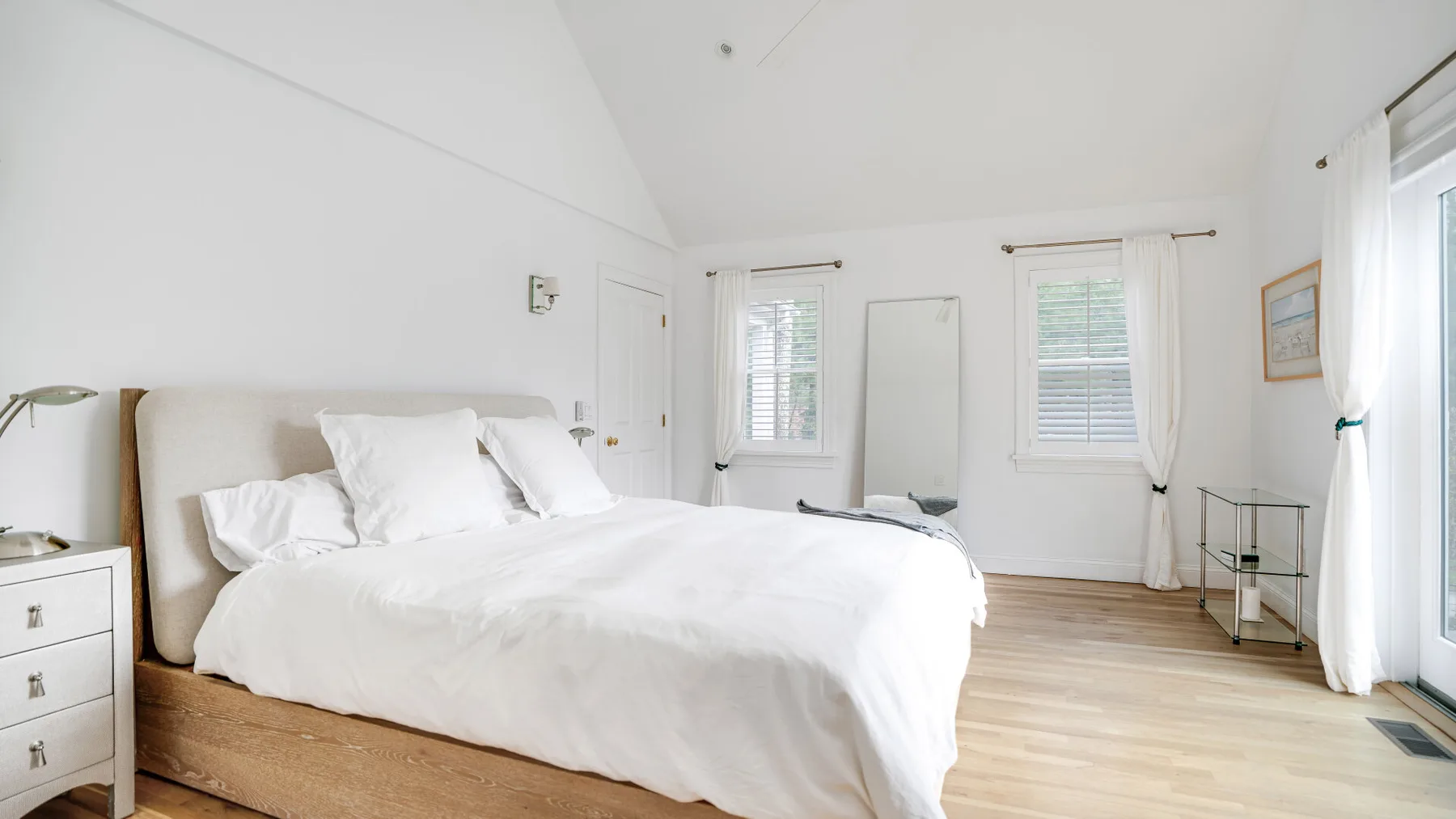 Un dormitorio luminoso con una cama grande y ventanas en la pared del fondo.