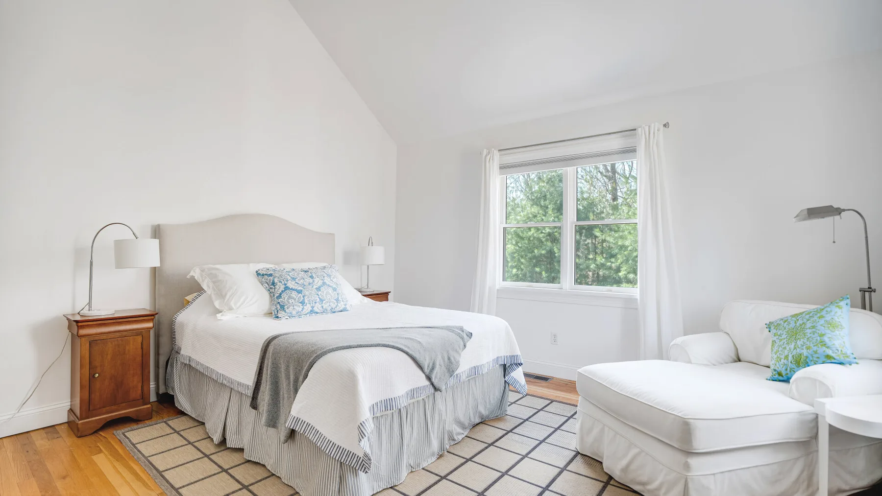 Un dormitorio con una cama, una ventana y una zona de asientos blanca.