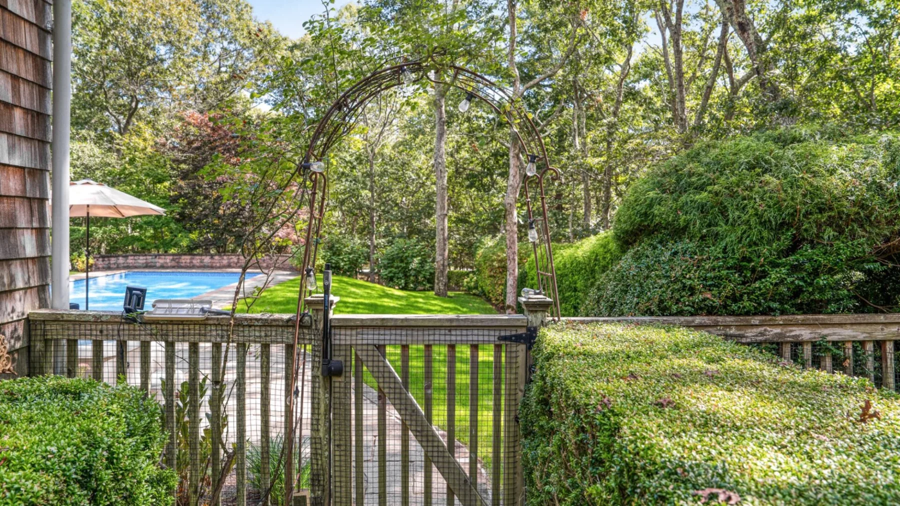 Una puerta de jardín da a un patio ajardinado con una piscina al fondo.