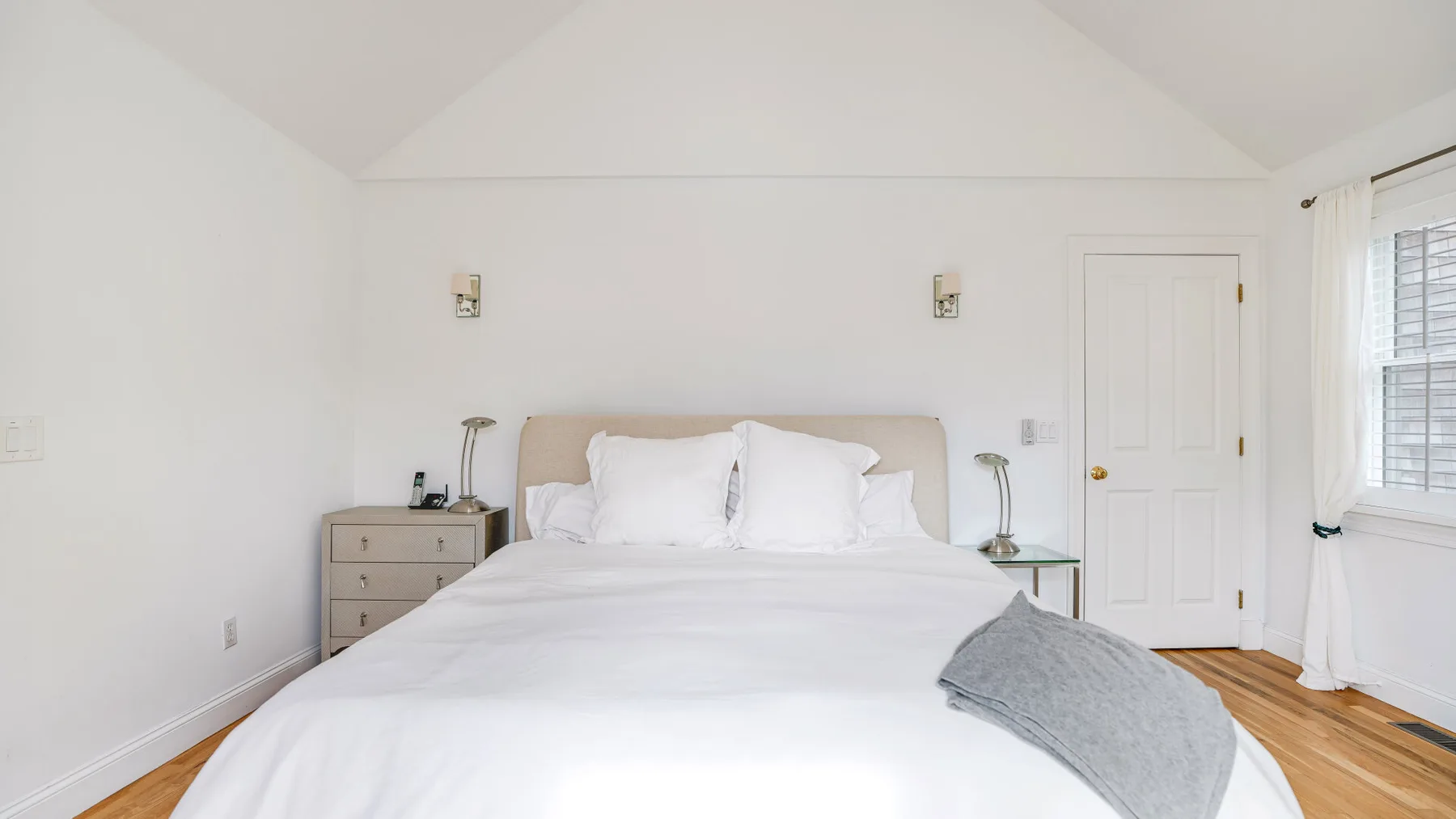 Un dormitorio luminoso con una cama bien tendida y una ventana con persianas.