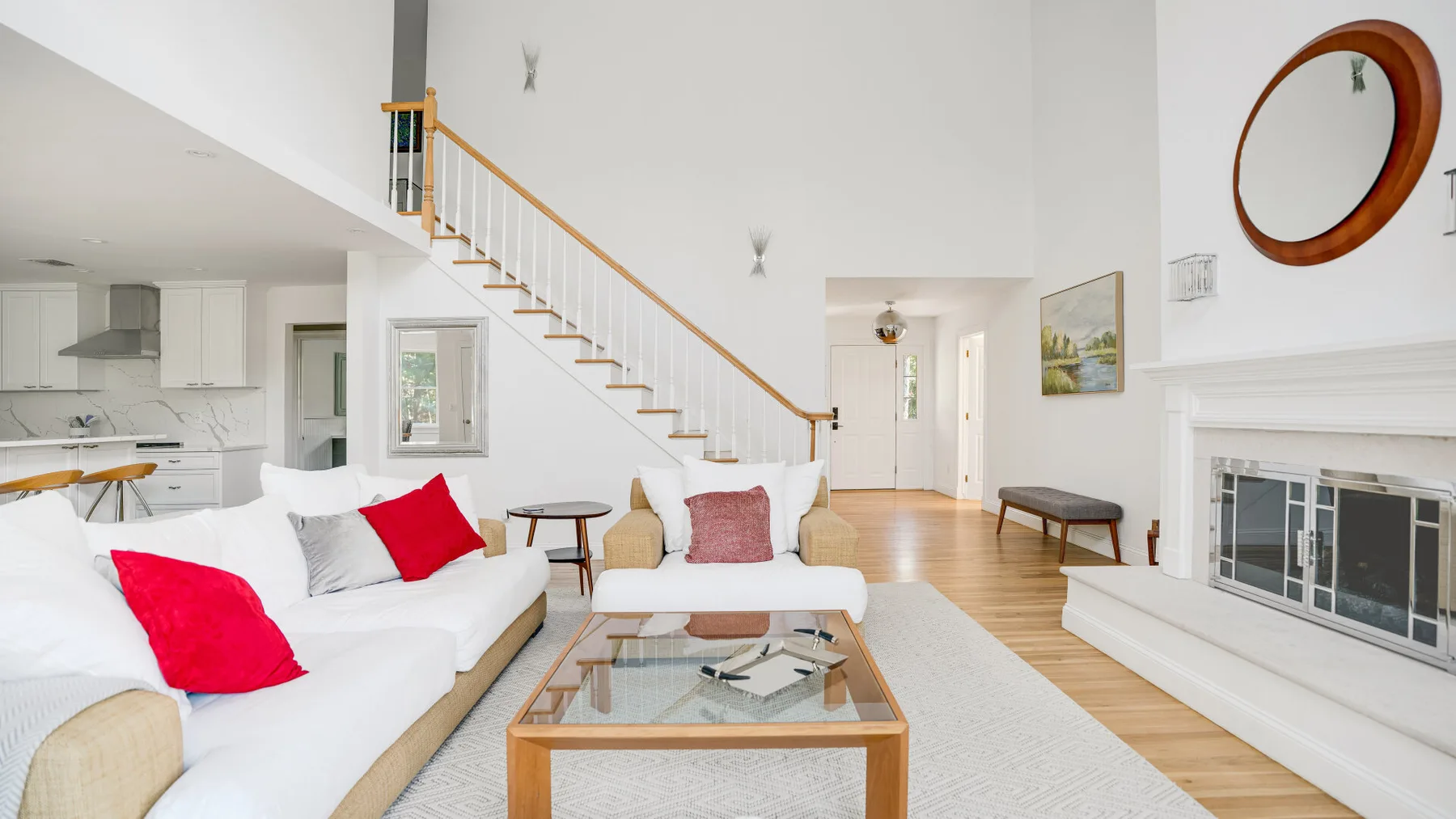 Una sala luminosa con asientos blancos, una mesa de centro de vidrio y escaleras.