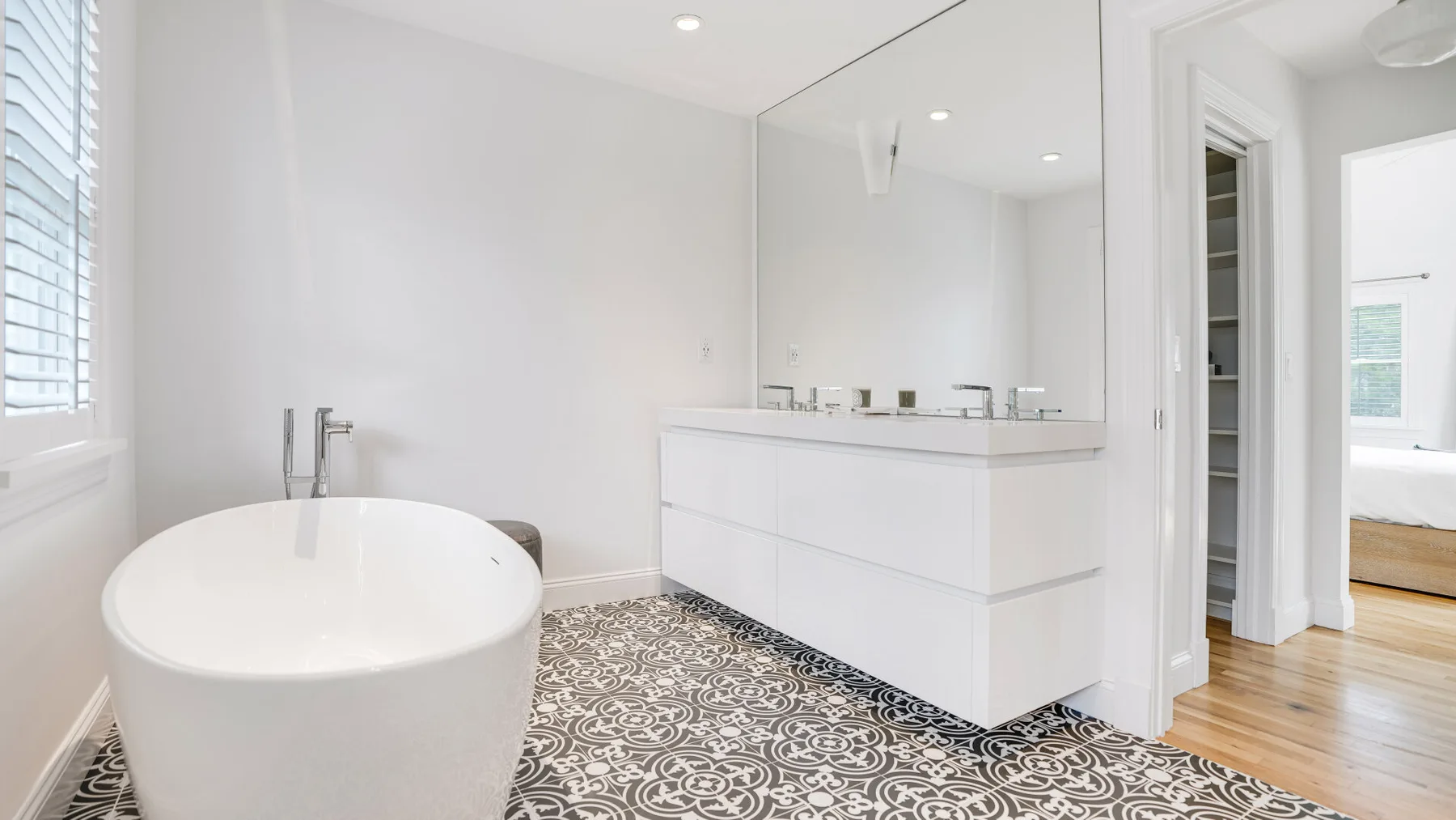Un baño luminoso con bañera exenta, tocador y suelo de baldosas estampadas.