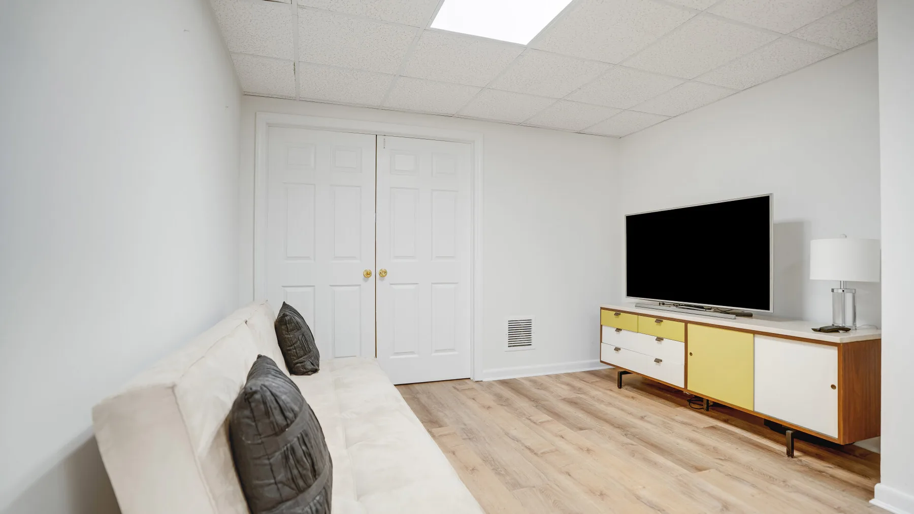 Una sala de estar luminosa con un sofá blanco y un televisor sobre un mueble bajo.