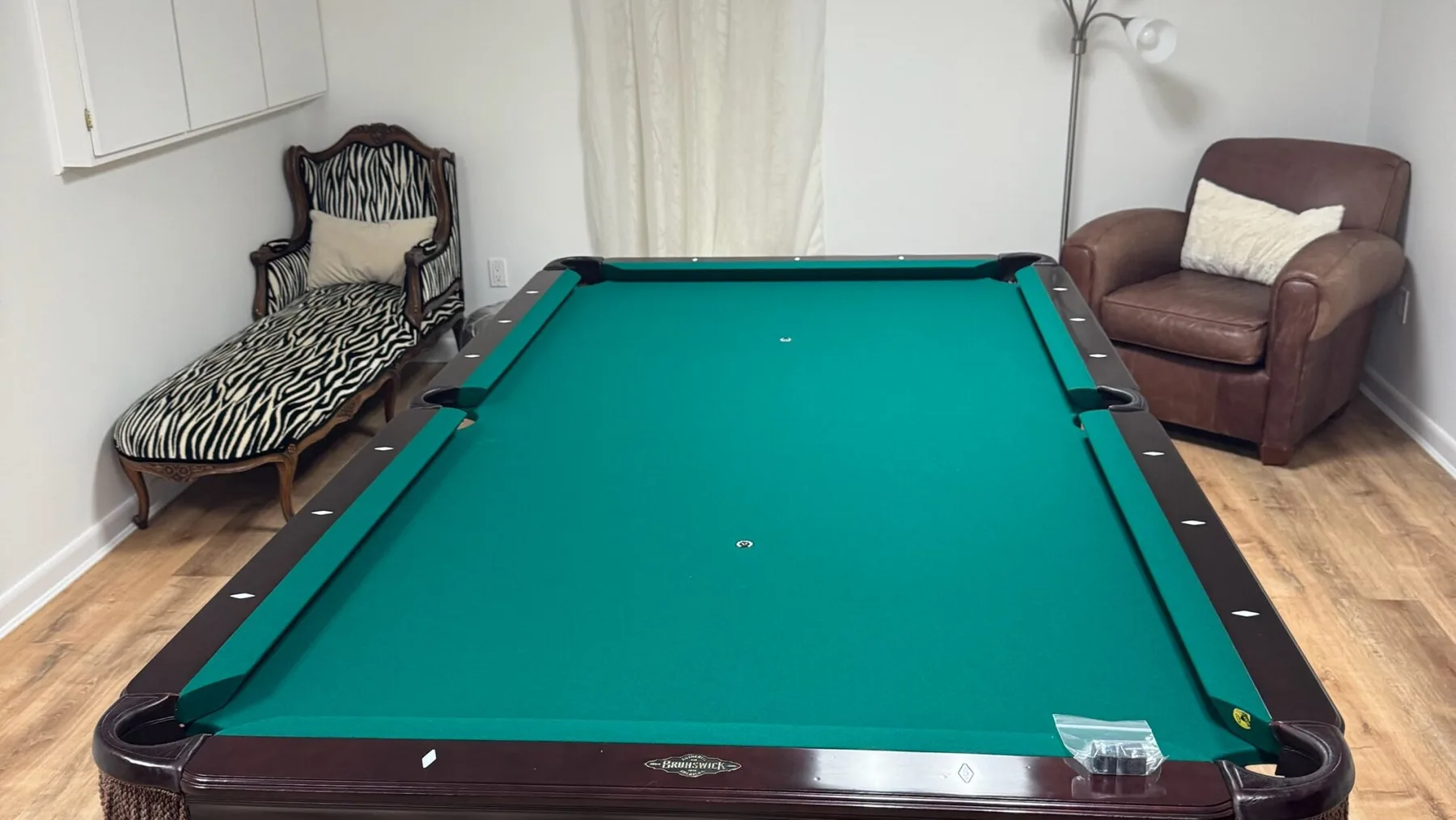 Una sala de juegos con una mesa de billar de paño verde y asientos junto a las paredes.