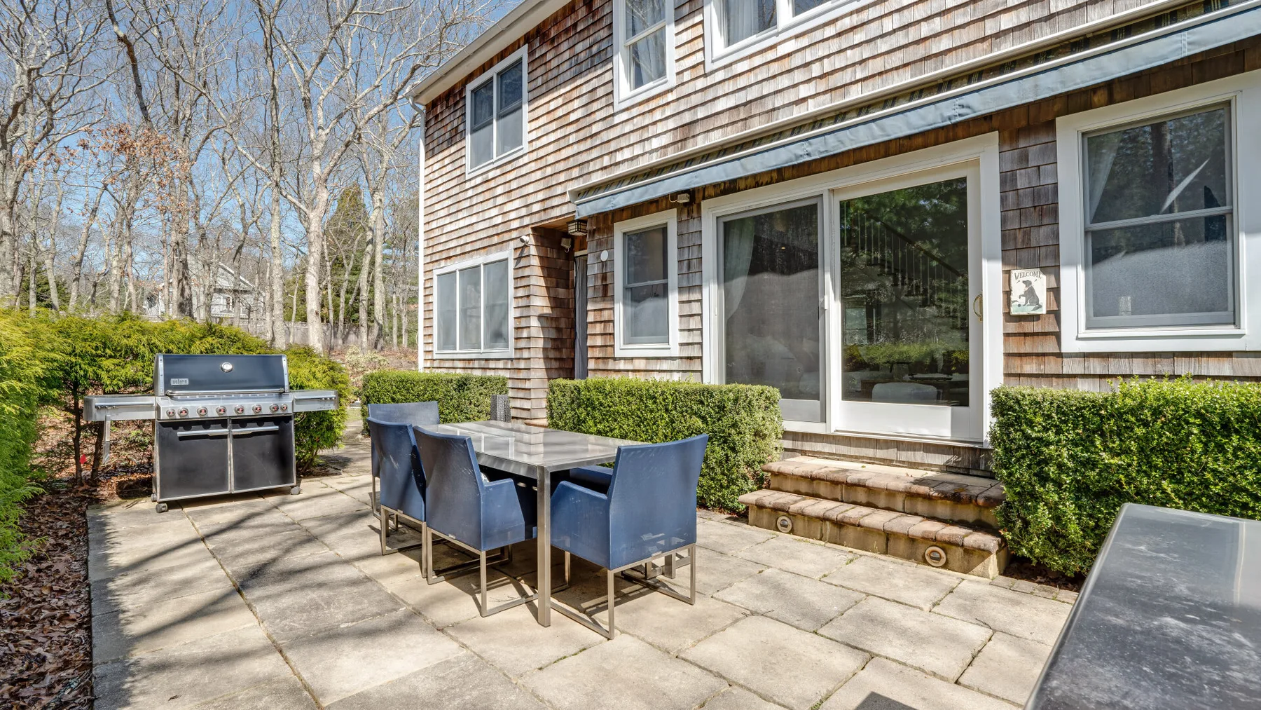 Un patio pavimentado tiene una mesa de comedor y asientos junto a la casa.