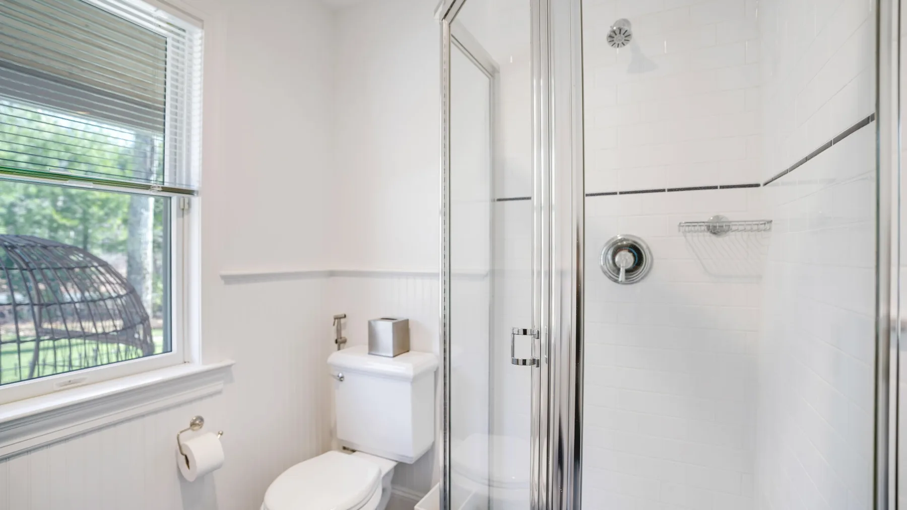 Un baño luminoso con una ducha de vidrio y una ventana.