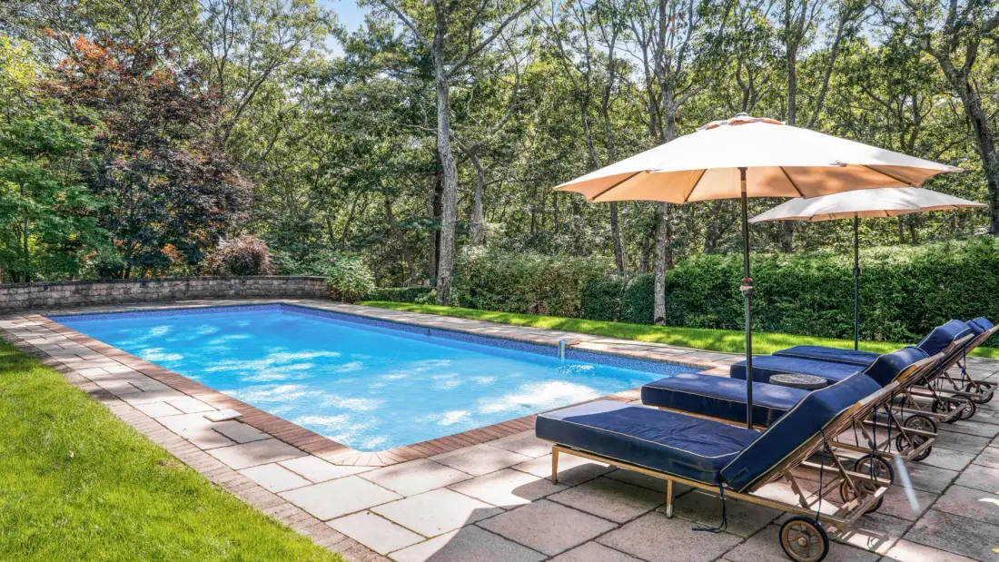 Una piscina al aire libre con asientos reclinables y una sombrilla a un lado.