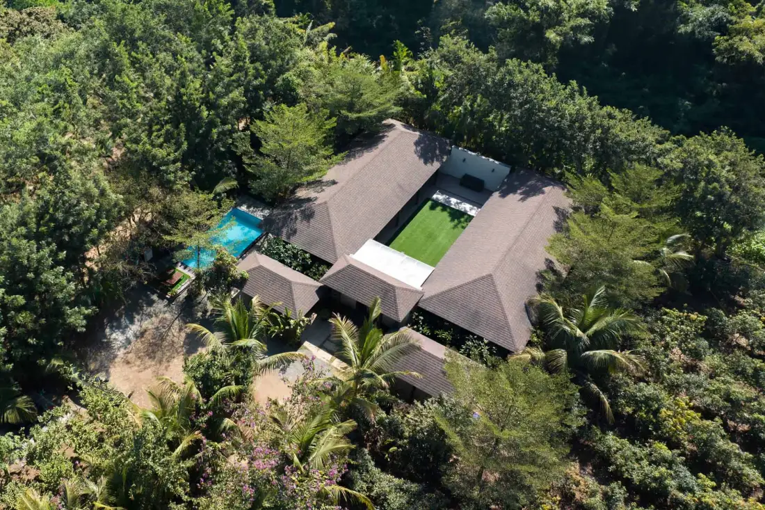 Vista aérea de una casa rodeada de vegetación densa, con una pequeña piscina cerca.