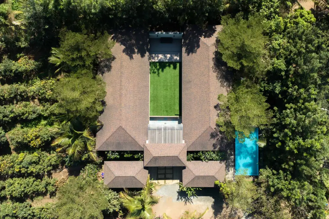 Vista aérea de una casa rodeada de árboles, con una piscina estrecha a un lado.