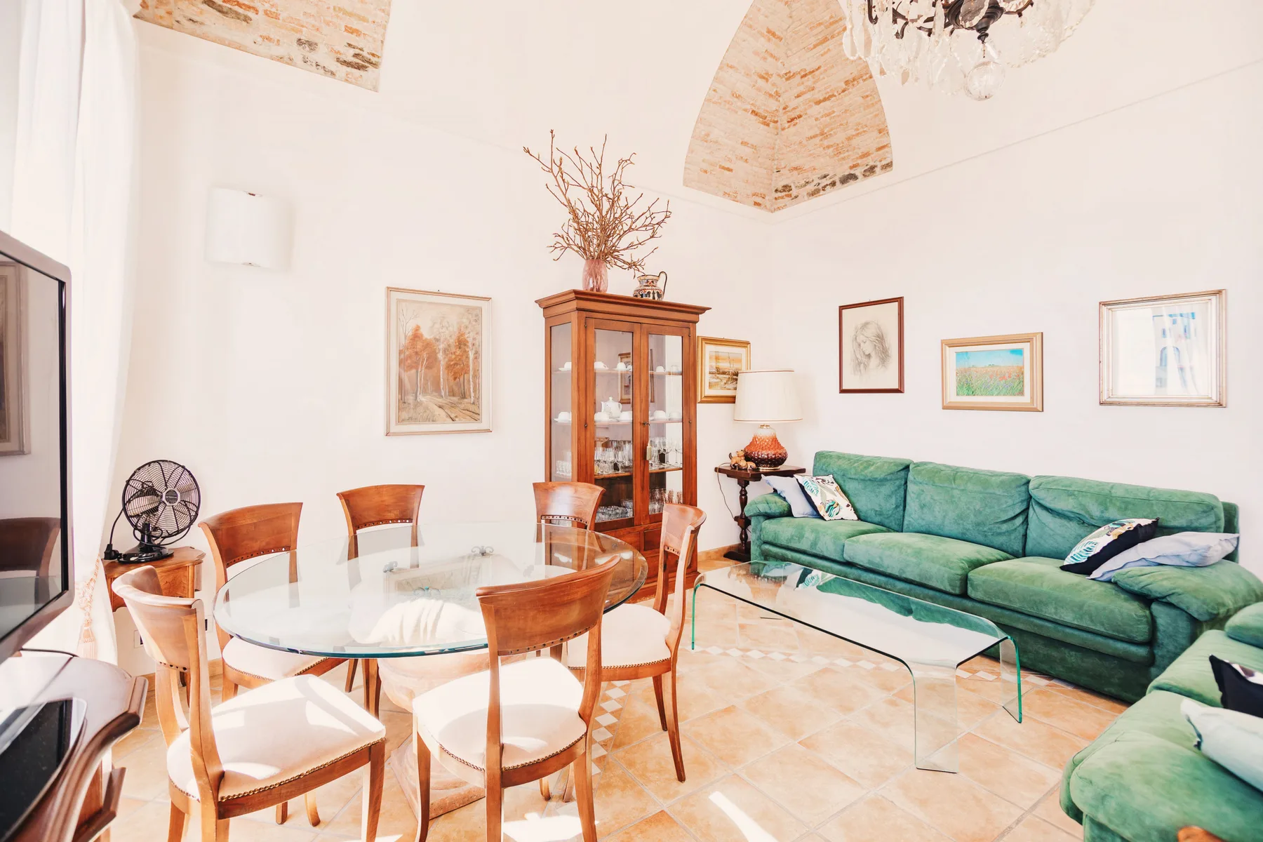 A bright living and dining room with green seating and a glass dining table.