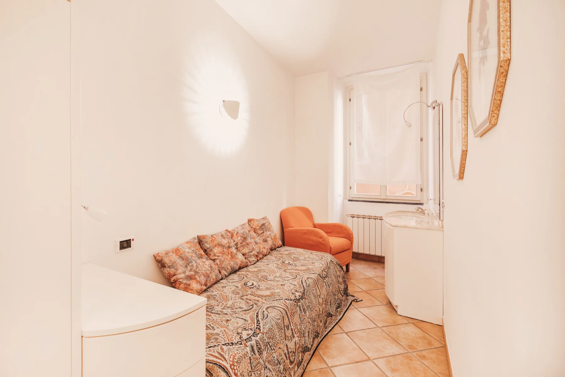 A small bedroom with a patterned bed, an armchair, and a window.