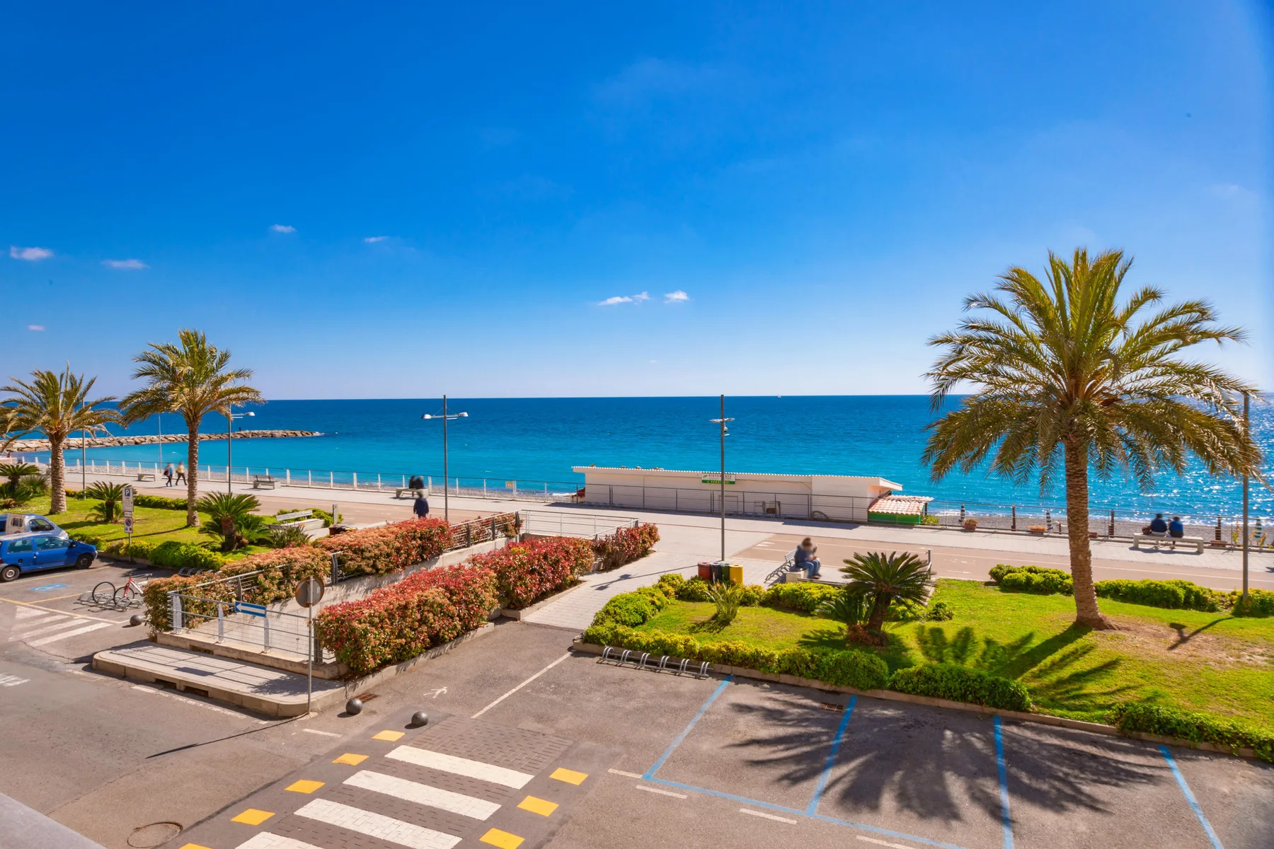 A seaside promenade overlooks the turquoise water, with palm trees lining the shore.