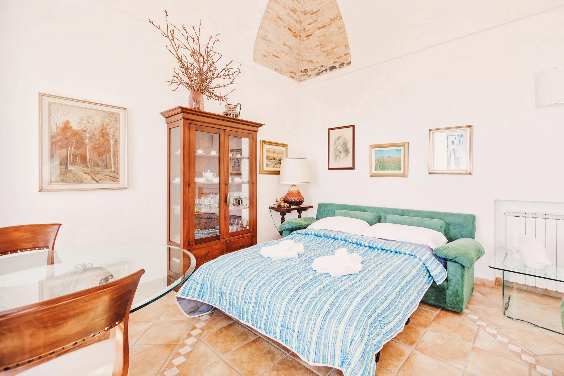 A bedroom with a bed dressed in blue and white bedding beside a green sofa.