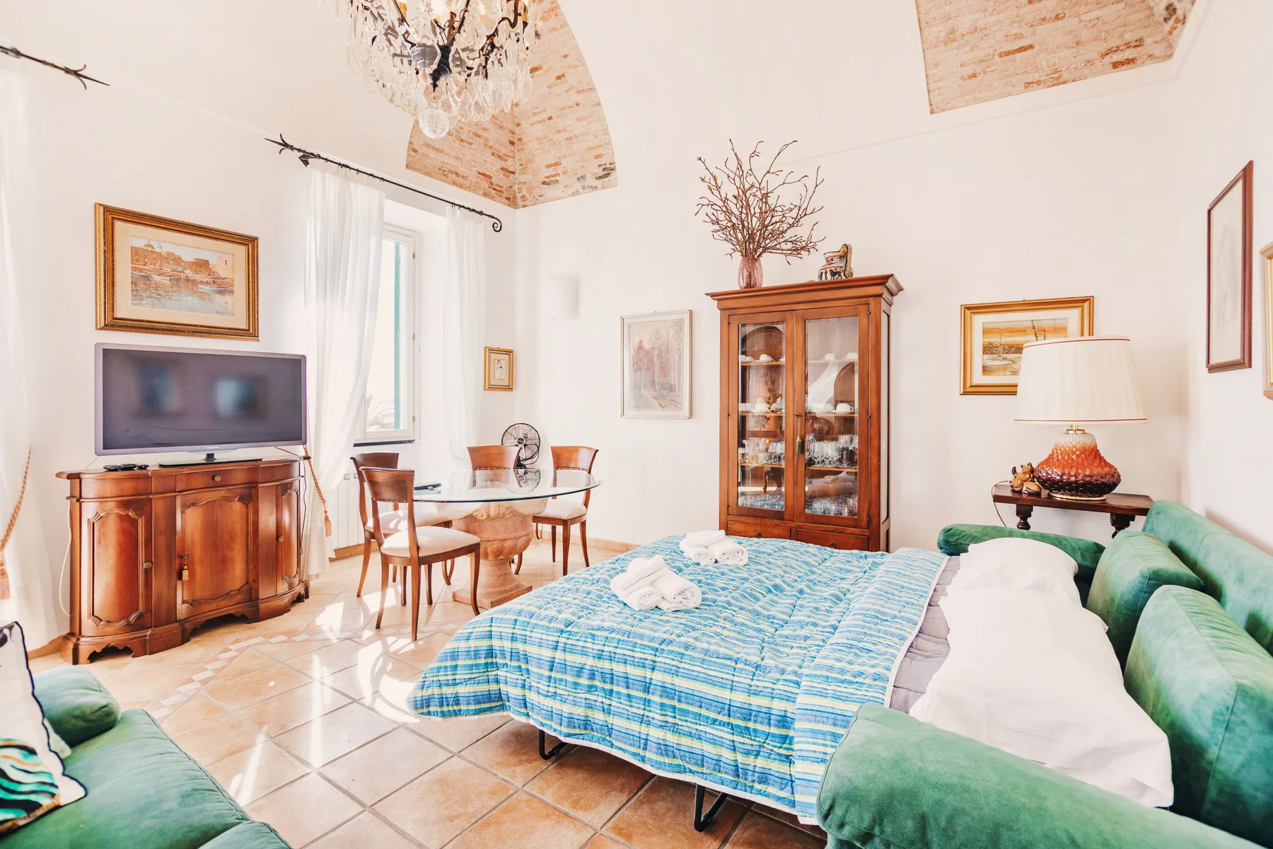 A bedroom with a blue-covered bed, green seating, and a wooden cabinet.