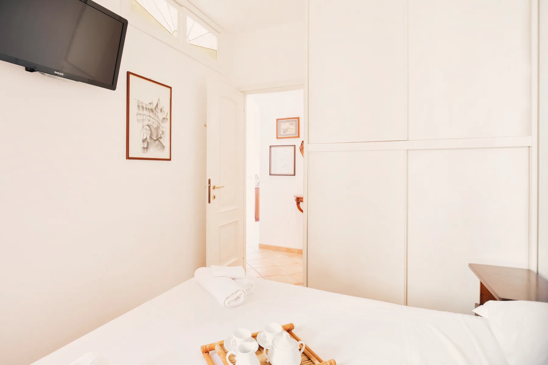 A bright bedroom with a bed, wall-mounted television, and framed artwork.