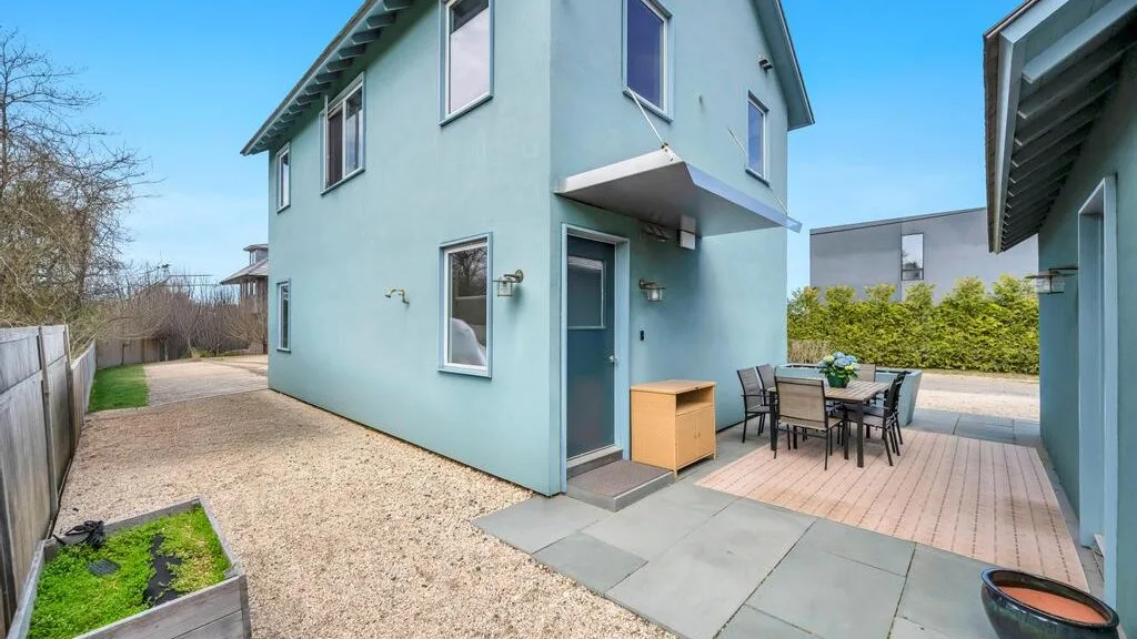 Una casa azul claro da a un patio pavimentado con asientos al aire libre.