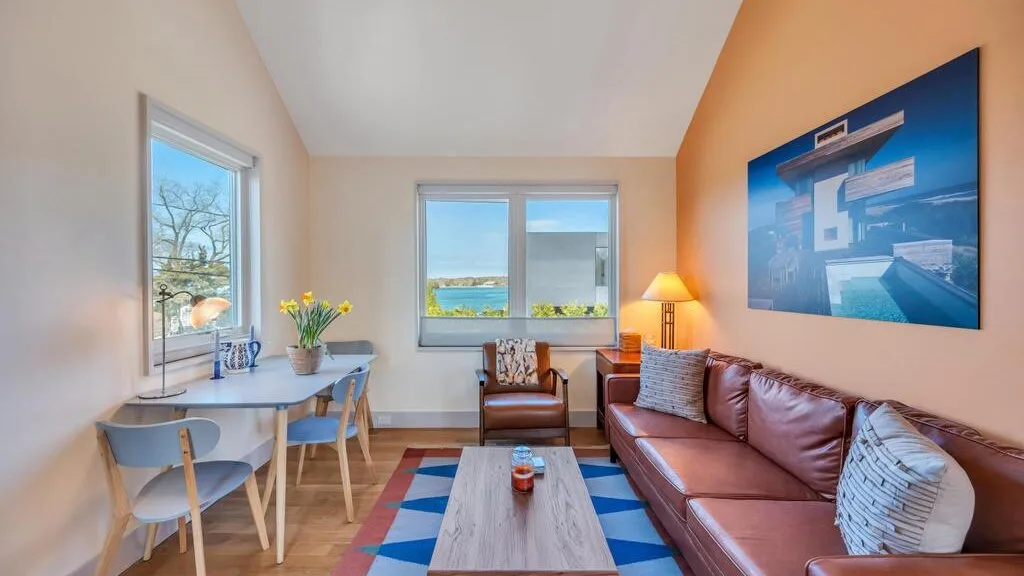 Una sala luminosa tiene una zona de asientos, una mesa de centro y ventanas grandes.