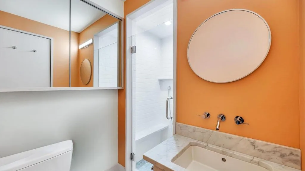 Un baño con una pared naranja, un espejo ovalado y un lavabo blanco.