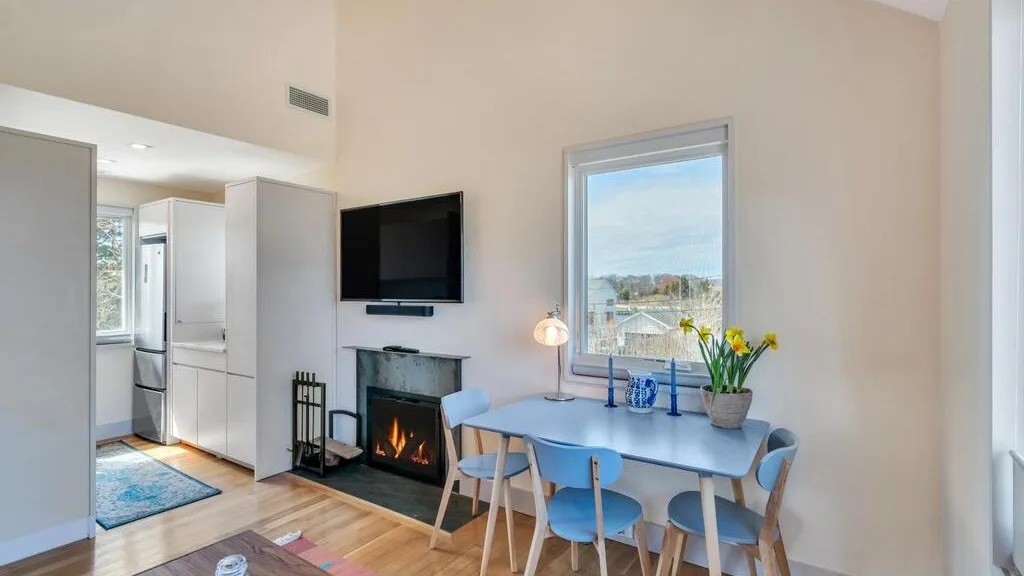 Un comedor luminoso con mesa y asientos junto a una ventana y una chimenea.