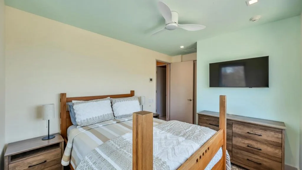 Un dormitorio con una cama de madera, ropa de cama estampada y un televisor en la pared.