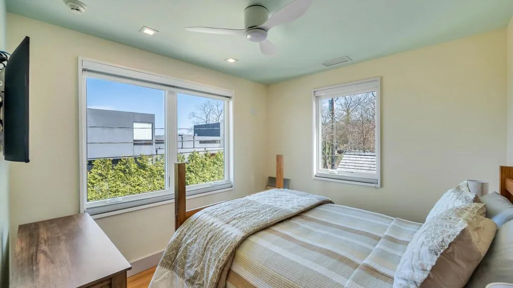 Dormitorio con una cama, ventilador de techo y ventanas con vistas a la vegetación.