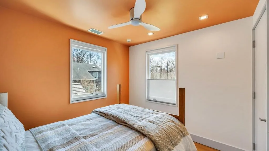 Un dormitorio con una cama bajo dos ventanas y un ventilador de techo.