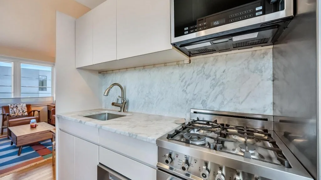 Una cocina compacta con encimera de aspecto marmolado, fregadero y cocina de gas.