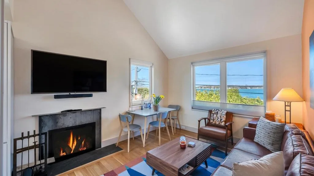 Una sala de estar con chimenea, asientos y grandes ventanas con vista al agua.