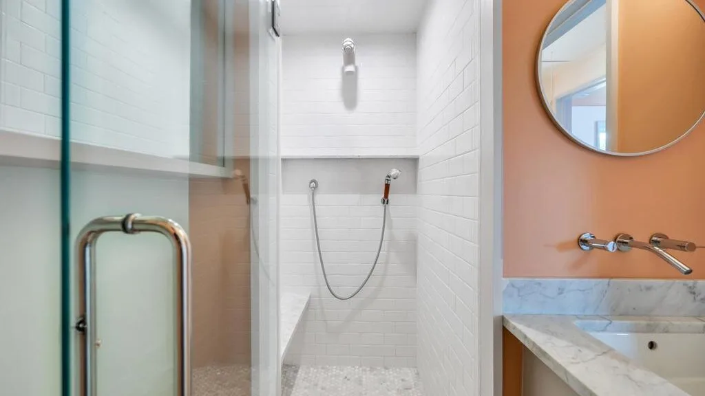 Una ducha de baño con azulejos, panel de vidrio y accesorios en la pared.