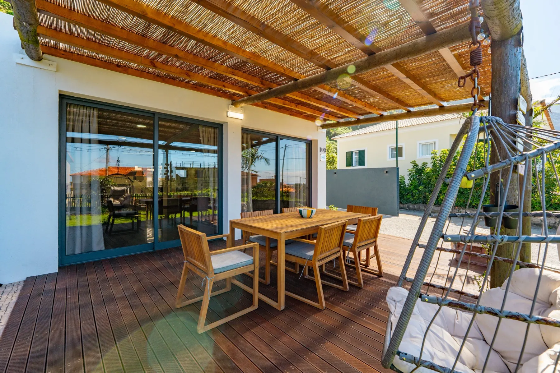 Covered outdoor deck with wooden table, chairs, and a hammock chair under a pergola.