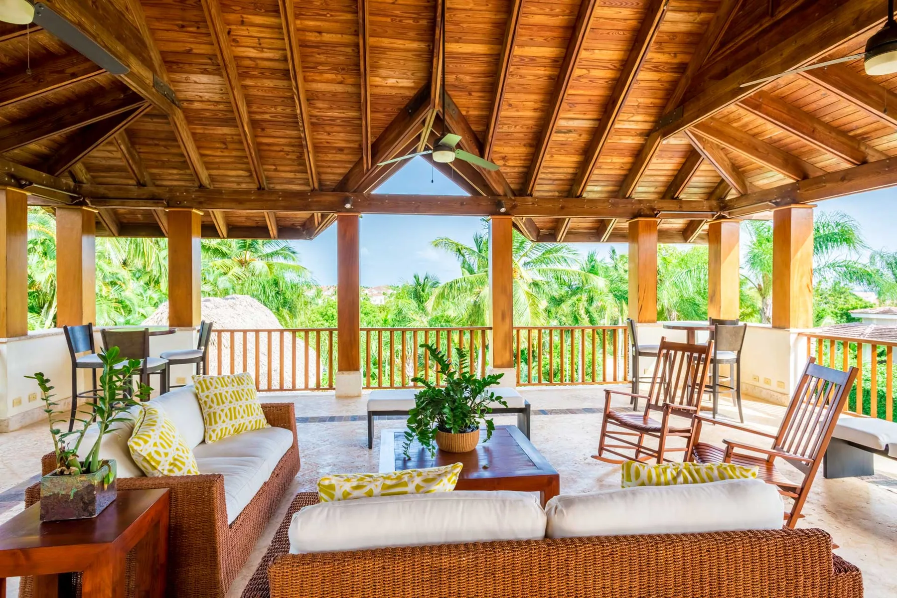 A covered outdoor lounge with seating, a table, and views of tropical greenery.