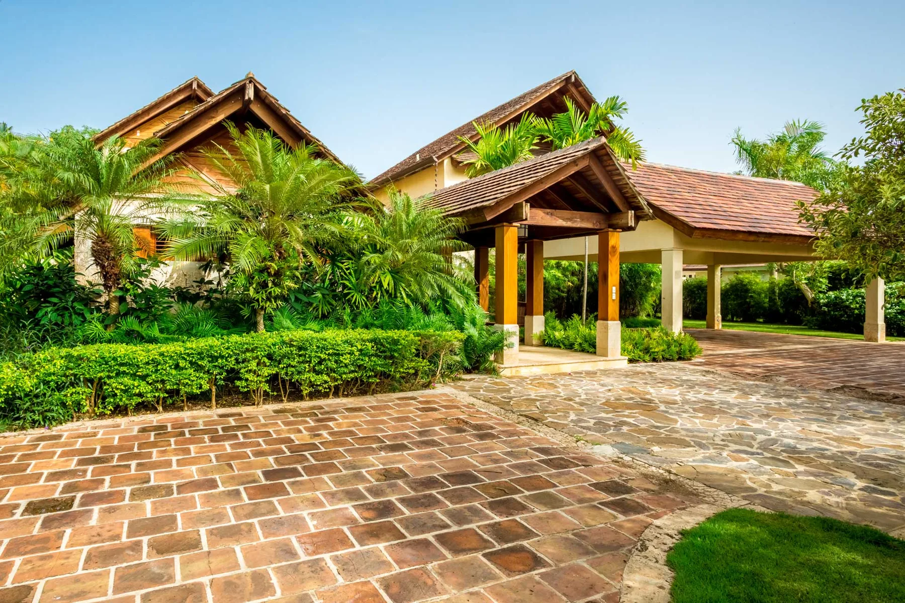 A tiled driveway leads to a covered entrance surrounded by tropical greenery.