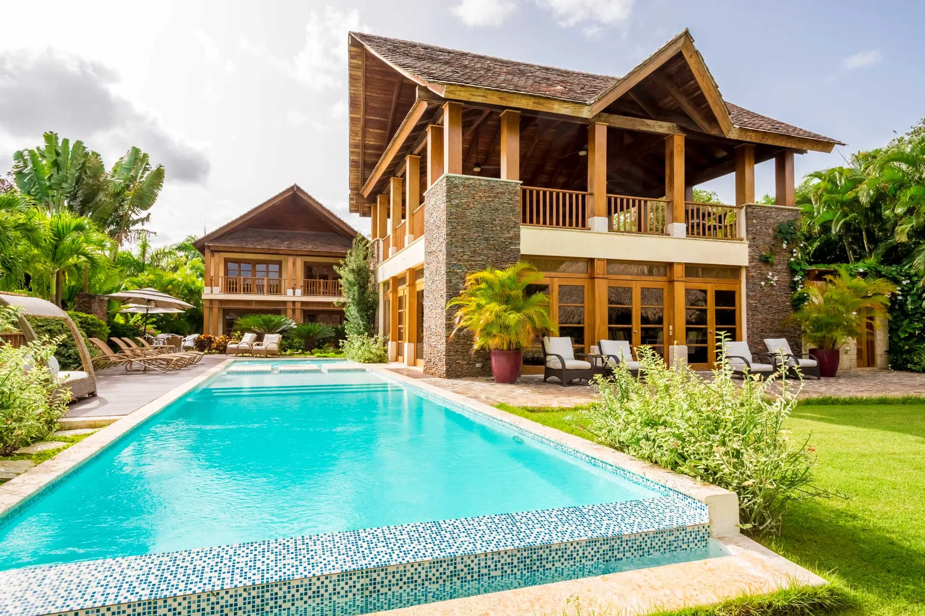A swimming pool in front of a large house with a covered balcony.
