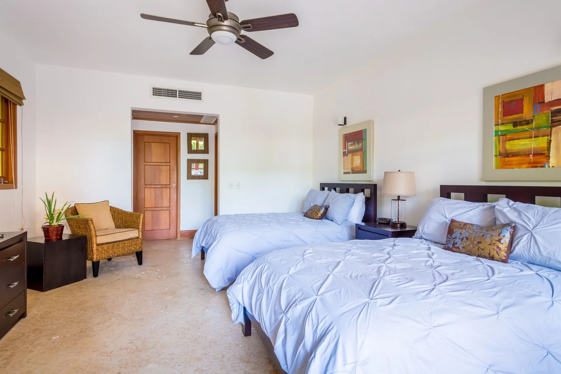 A bedroom with two beds, a ceiling fan, and framed artwork.