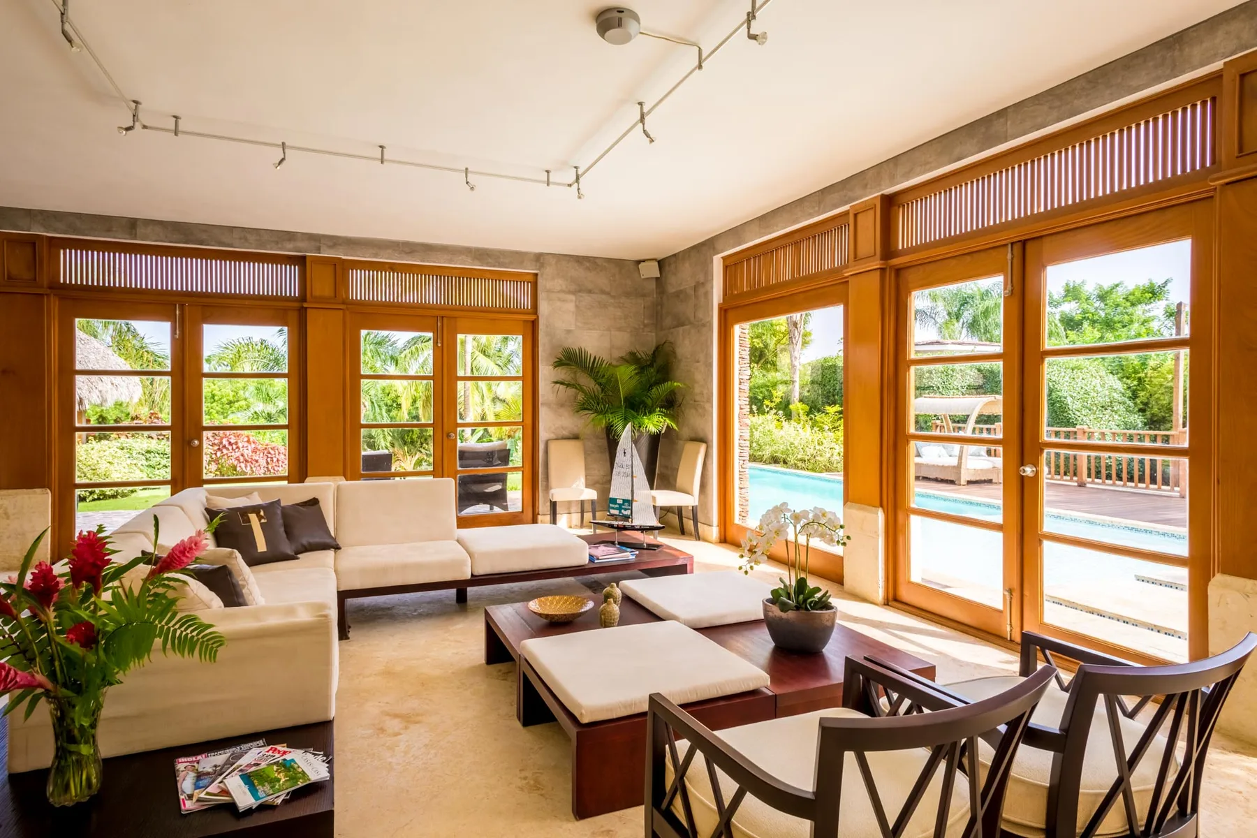 A bright living room with seating beside large windows overlooking a pool.