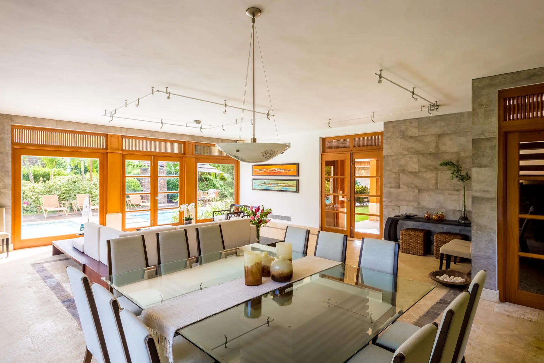 A bright dining and living area has a glass dining table and broad garden-facing windows.