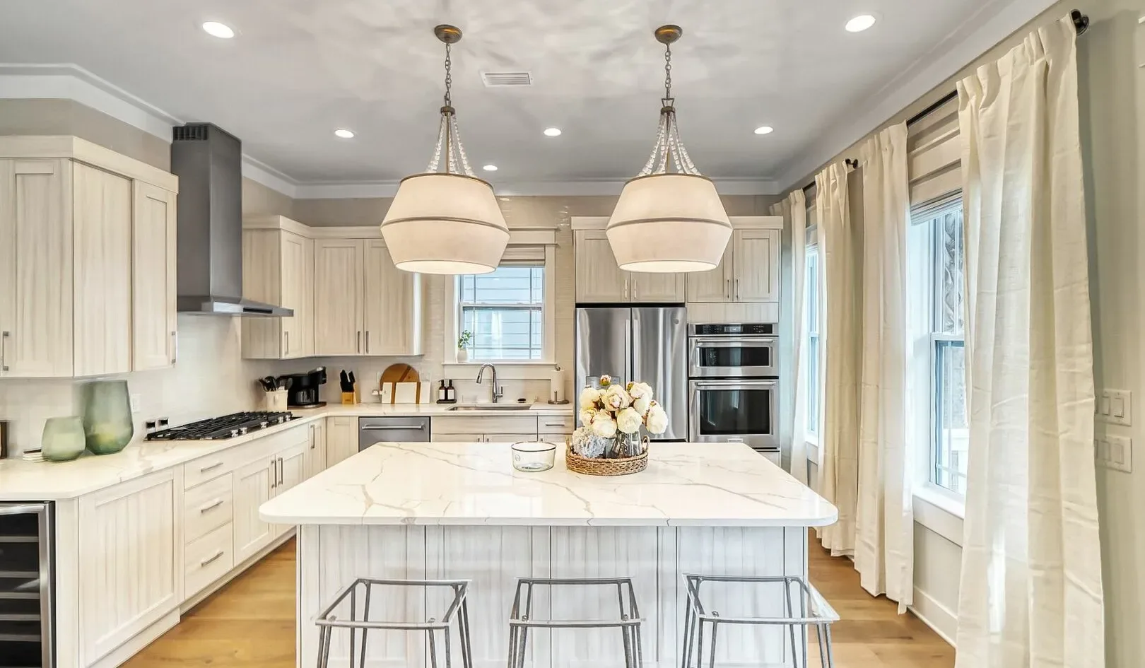 A bright kitchen with pale cabinetry, a large island, and pendant lights.