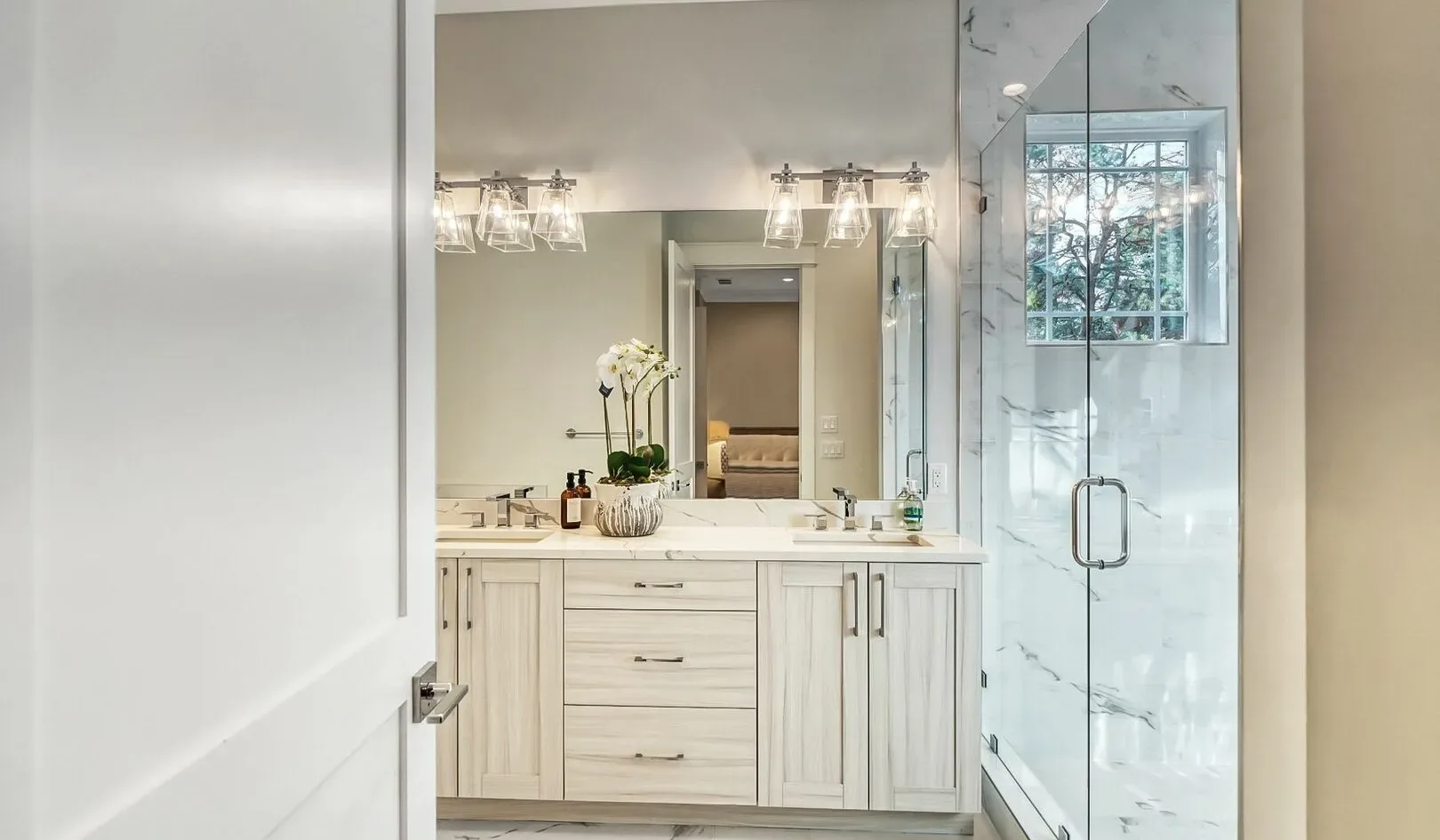 A bright bathroom with a vanity, mirror, and glass shower.