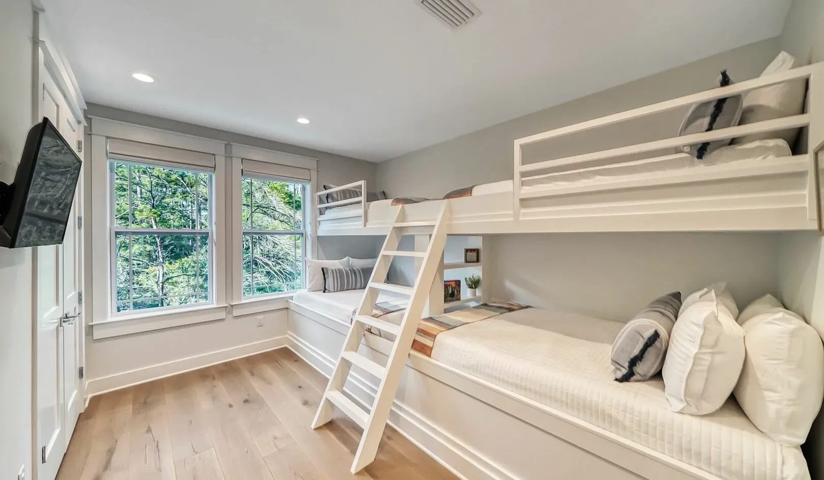 A bedroom with a white bunk bed, ladder, and large windows.