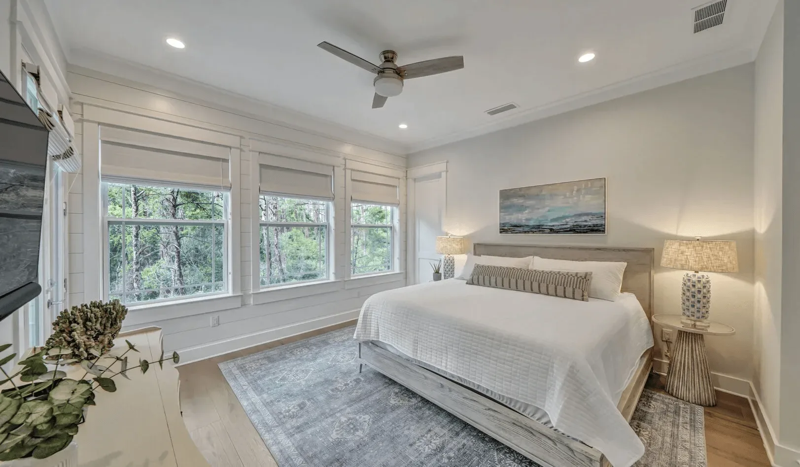 A bright bedroom features a neatly made bed beside large windows.
