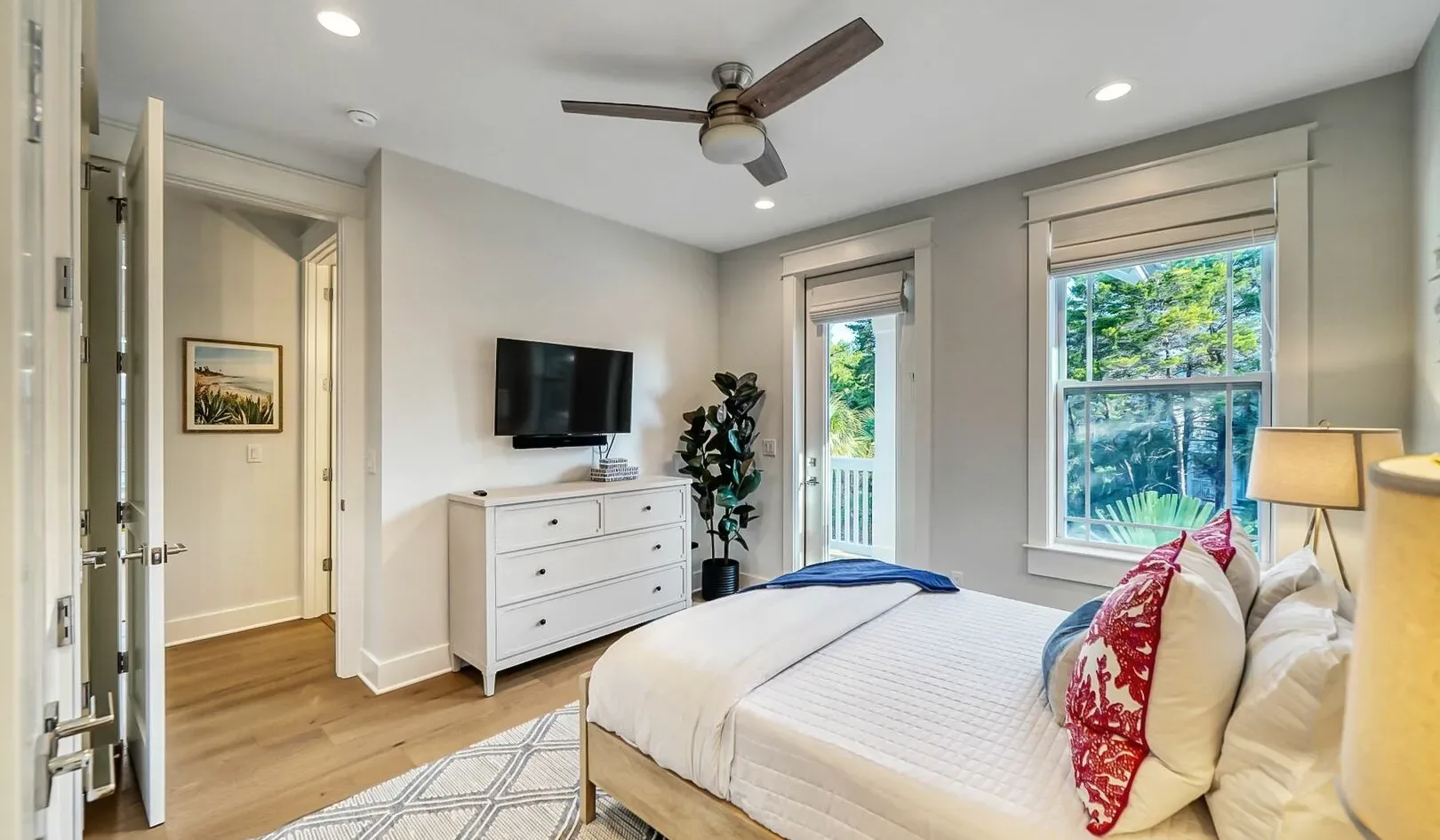 A bright bedroom with a neatly made bed and dresser beneath a wall-mounted television.