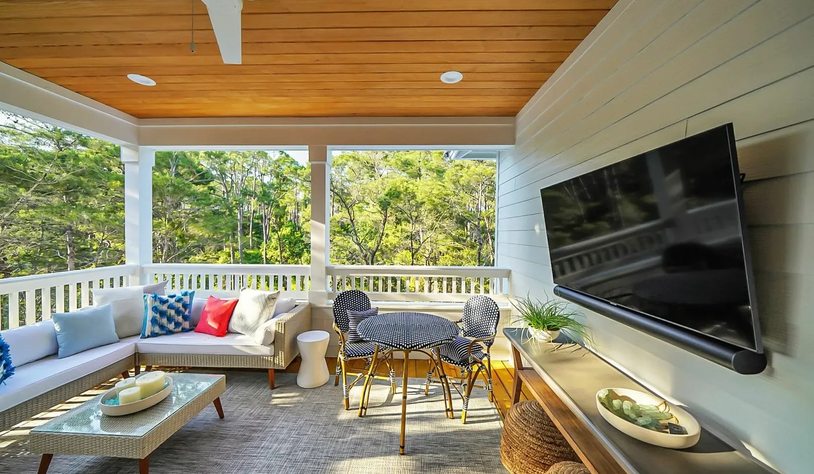 A bright covered patio with seating, a dining table, and a wall-mounted television.