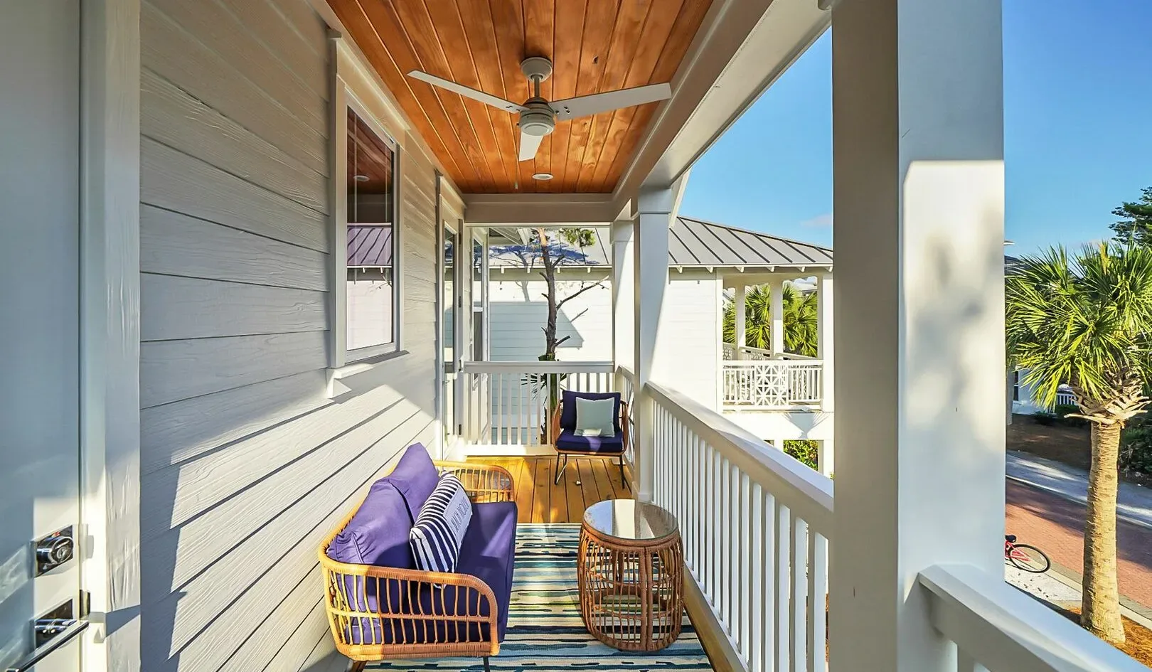 A covered porch with seating, a ceiling fan, and views of nearby greenery.