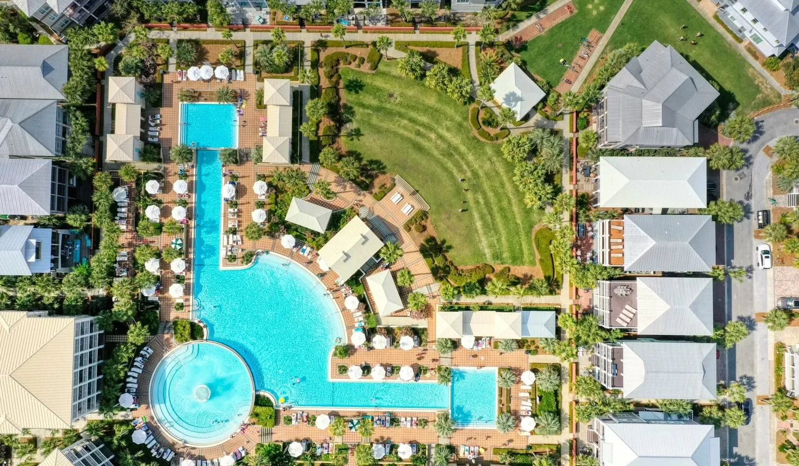 Una vista aérea muestra un complejo de piscinas rodeado de jardines y edificios.