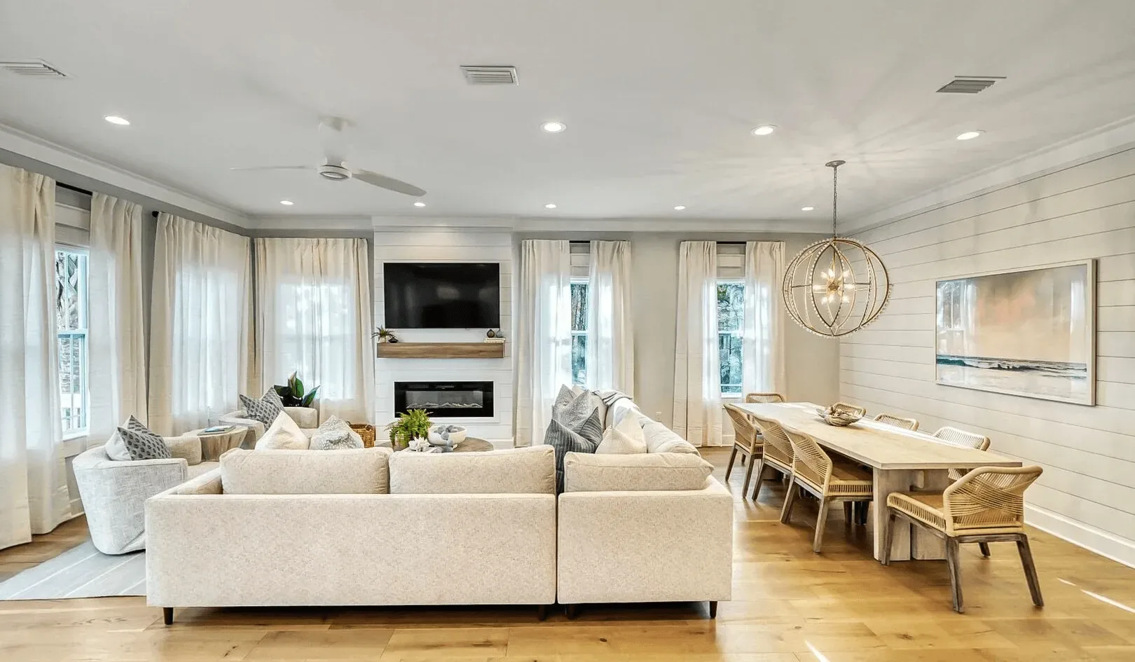 A bright living and dining area has light seating, a television, and a dining table.