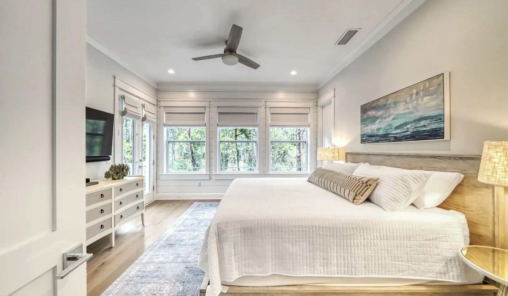 A bright bedroom with a large bed, several windows, and a ceiling fan.