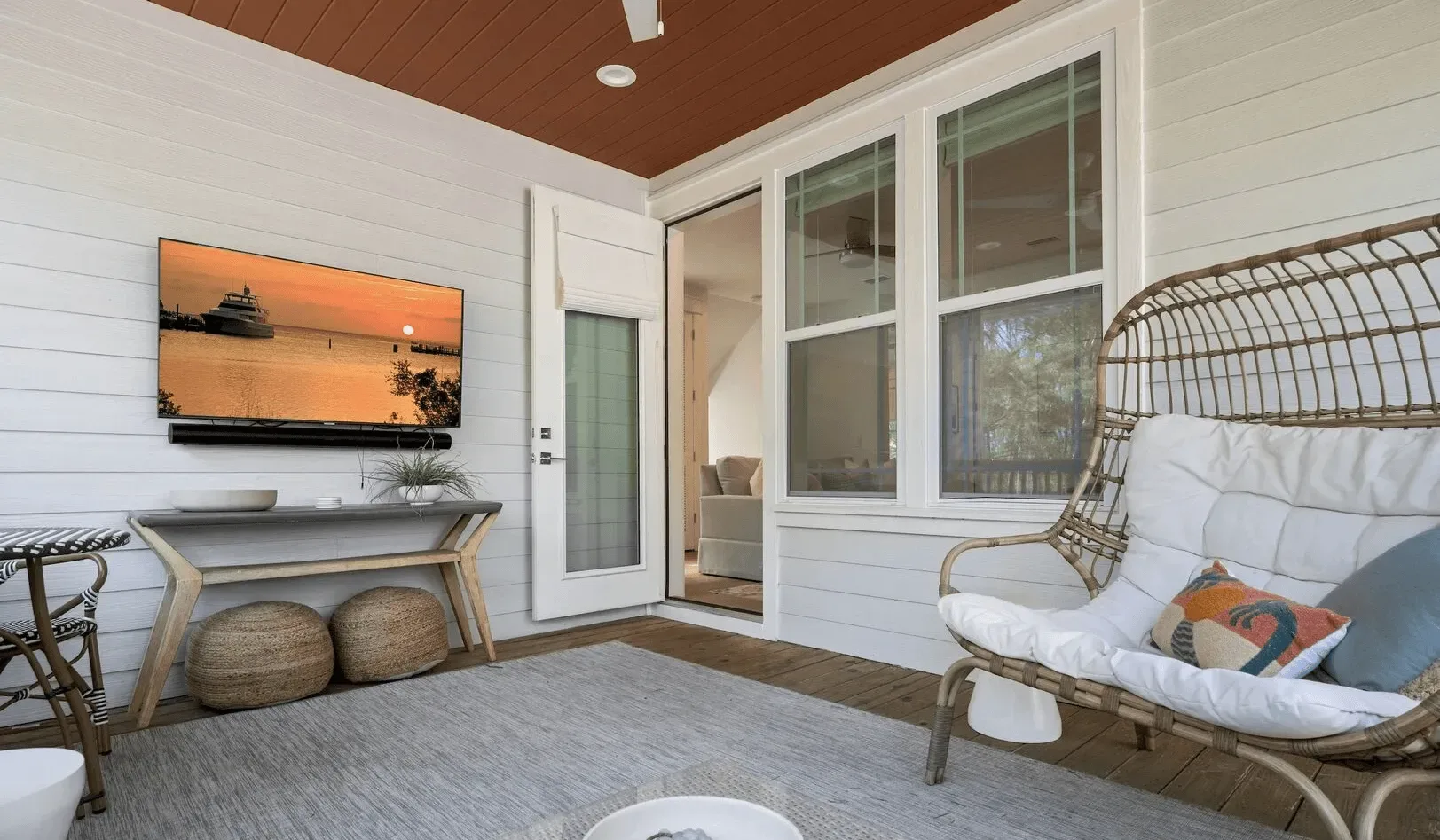 A sunroom with a cushioned wicker seating area and large windows.